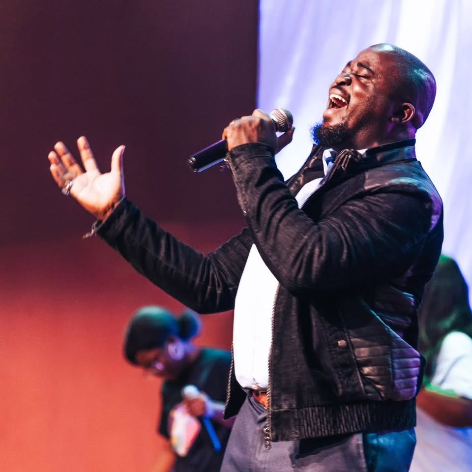 Soji Akinleye singing on stage, hand raised in worship