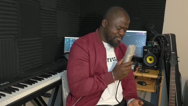 Soji recording vocals in a home studio, wearing a burgundy jacket